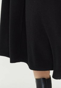 Schwarzes Strickkleid mit ausgestelltem Design, das eine glatte Textur und klare Linien aufweist. Betont durch einen stilvollen schwarzen Stiefel am unteren Rand.