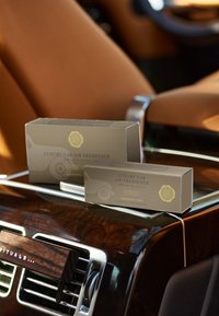 Två bruna lådor med "Luxury Car Air Freshener" märkta "Cashmere Rose" placerade på en träpanel vid sidan av en metallisk luftventil.