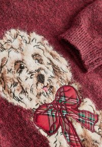 Burgunderfarbener Strickpullover mit einer strukturierten beigen Hundillustration und einem roten und grünen Karobanddetail im unteren Bereich.