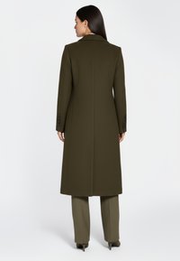 Lange olijfgroene jas met een gestructureerd ontwerp, textuurrijk materiaal, kraag met inkeping en manchetten met vier knopen, gecombineerd met bijpassende broek.