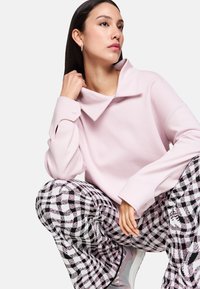 Light pink sweatshirt with a high collar and buttoned cuffs, paired with black and white checkered pants and light pink athletic shoes.