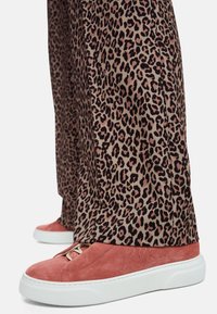 Pink suede sneakers with white soles, laces, and subtle branding, paired with brown leopard print, wide-legged trousers.