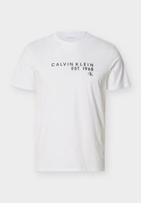 Λευκό κοντομάνικο T-shirt με μαύρο κείμενο «CALVIN KLEIN EST. 1968» και μικρό λογότυπο «CK» στο επάνω μέρος του στήθους.