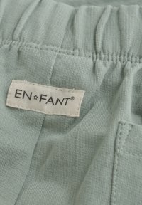 Ljusgrönt tyg med en mjuk textur, med en gathered midja och en tygetikett som säger "EN·FANT" i svart på en beige bakgrund.