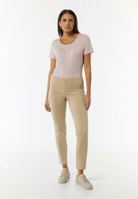 Helles rosa T-Shirt mit kurzen Ärmeln, kombiniert mit beigen, figurbetonten Hosen und beigen Sneakers, die über einen elastischen Bund für Komfort verfügen.