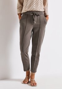 Pantaloni sportivi grigi a sigaretta con righe laterali, vita elasticizzata, cordino e due tasche laterali. Abbinati a sandali piatti color sabbia.