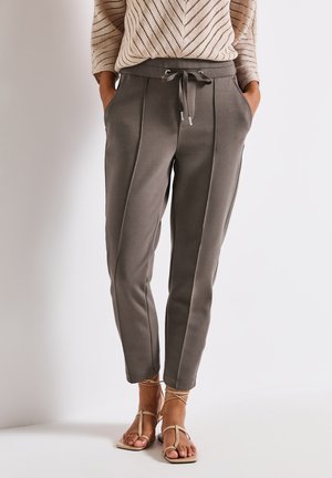 Graue, schmal zulaufende Sweatpants mit seitlichen Streifen, elastischem Bund, Kordelzug und zwei seitlichen Taschen. Dazu werden beige flache Sandalen getragen.