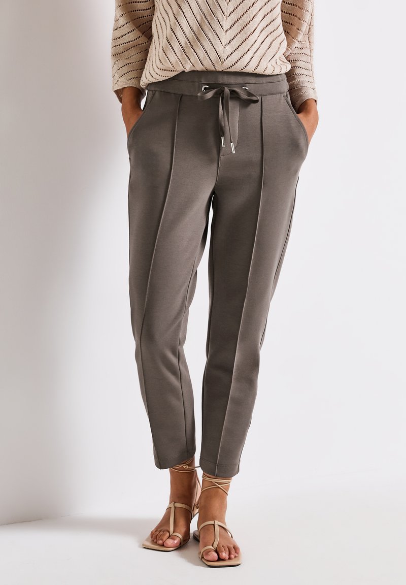 Pantaloni sportivi grigi a sigaretta con righe laterali, vita elasticizzata, cordino e due tasche laterali. Abbinati a sandali piatti color sabbia.