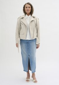 Hellbeige Lederbikerjacke über einem weißen Hemd mit Knopfleiste, kombiniert mit einem Jeansrock mit einem Schlitz vorne und nacktfarbenen Blockabsatzsandalen.