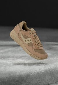 Sportski tenisica sa bež gornjim dijelom od brušene kože i mrežastog materijala, teksturiranim detaljima, vezicama i gumenim potplatom sa istaknutim dizajnom logotipa sa strane.