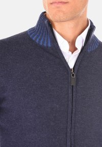 Maglione navy con zip, dettagli a coste blu, realizzato in materiale a maglia testurizzato. Presenta una cerniera frontale e colletto ripiegato.