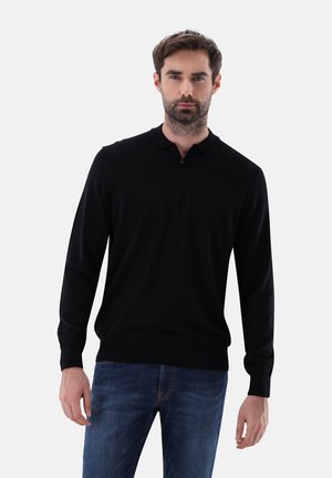 Schwarzer Langarm-Polo-Pullover aus Strickstoff, mit einem halben Reißverschluss, Kragen und taillierten Bündchen, getragen mit blauen Jeans.