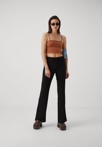 Cropped orange patterned top with thin straps, black flared pants, and brown clogs. Small blue handbag and black sunglasses complete the look.