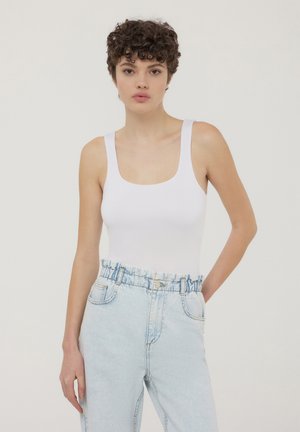 Body bianco senza maniche con scollatura quadrata, abbinato a jeans a vita alta blu chiaro con elastico in vita e tasche.