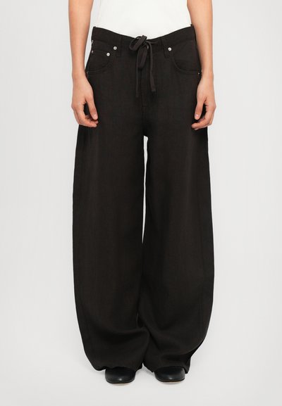Pantalons larges noirs en tissu texturé, avec une taille à cordon de serrage, des poches avant et des accents en métal argenté.