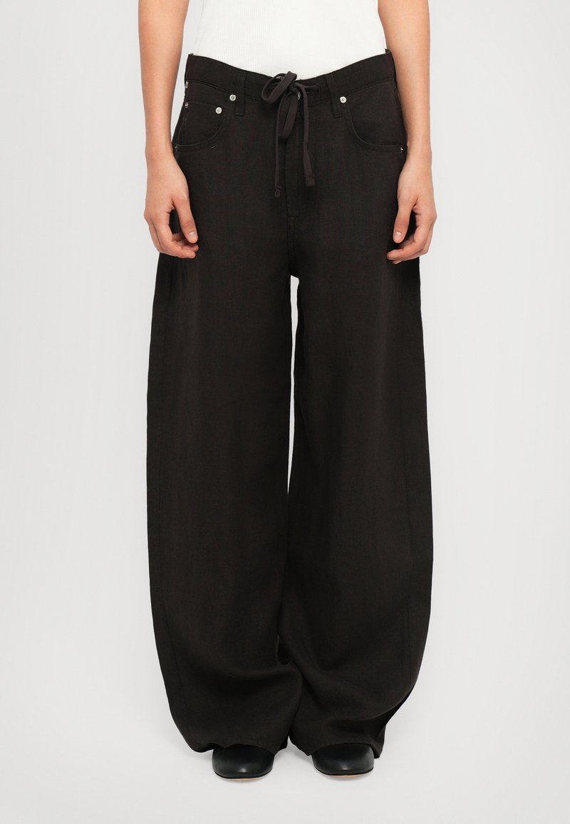 Pantalones negros de pierna ancha hechos de una tela texturizada, con cintura ajustable mediante cordón, bolsillos frontales y detalles de hardware en tono plateado.