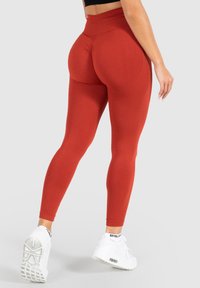 Leggings a vita alta e aderenti di un ricco colore rosso con un motivo testurizzato. Abbinati a scarpe da ginnastica bianche con un logo.