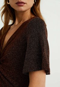 Glänsande brun klänning med djup V-ringning och korta ärmar; har texturerad tyg med subtil glittrande effekt och en omslagdesign.