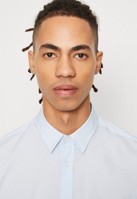 Himmelblaues Hemd mit klassischem Kragen, glattem Stoff und dezentem Glanz. Verfügt über eine Frontleiste mit perlmuttfarbenen Knöpfen.