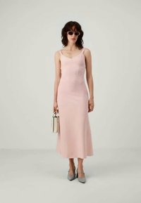 Abito aderente rosa chiaro con spalline sottili, di lunghezza media, con una texture sottile; abbinato a scarpe grigie e una piccola borsa bianca.