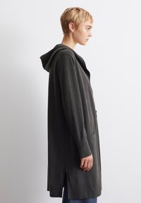 Mørkegrå lang cardigan med hette, sidespalter og lommer. Myk tekstur, lange ermer, avslappet passform. Minimalistisk design, ingen synlige mønstre.