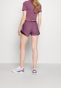 Conjunto deportivo morado con detalles negros, hecho de tela suave. Zapatillas blancas con detalles morados completan el atuendo.