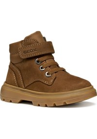 Botines de ante marrón con suela de goma, que cuentan con una correa de velcro y un diseño de cordones. Incluyen ojales de metal y detalles cosidos.