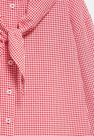 Chemise à carreaux vichy rouge et blanche avec boutons sur le devant et un détail en tissu noué au col.