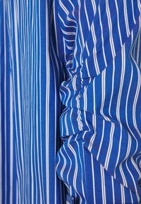 Tessuto a strisce blu e bianche con volant lungo la cucitura. Il tessuto ha una texture liscia e un colore vivace, con strisce sottili e spesse.