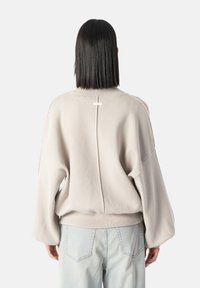 Suéter beige de corte oversize con hombros caídos, puños acanalados y un sutil detalle de costura central. Textura suave, combinado con jeans de denim claros.