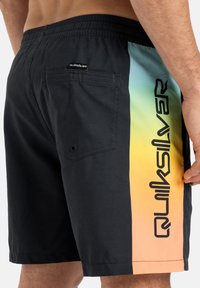 Schwarze Schwimmshorts mit einem seitlichen Farbverlauf von Cyan zu Orange, versehen mit einem vertikal aufgedruckten schwarzen Logo. Enthält eine Gesäßtasche und einen elastischen Bund.