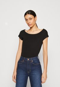 Tricou negru, mulat, cu decolteu larg și mâneci scurte, asociat cu blugi din denim albastru închis, cu talie înaltă și buzunare frontale.
