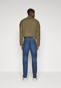 Olive green shirt with a relaxed fit, paired with blue denim jeans featuring a straight cut and subtle detailing on the back pockets.