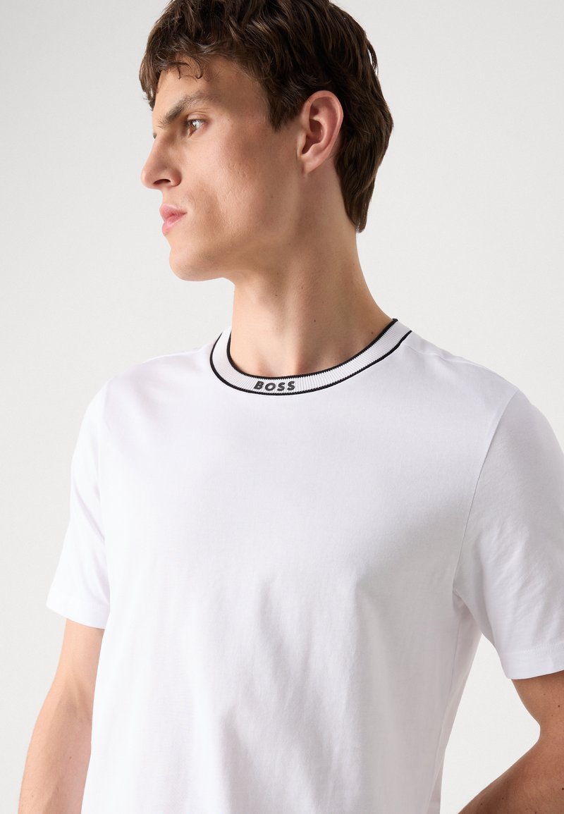 Weißes Baumwoll-T-Shirt mit kurzen Ärmeln, kontrastierendem schwarzen Ripp-Halsausschnitt, mit dem aufgestickten "BOSS"-Logo am Kragen. Schlichtes, strukturiertes Design.