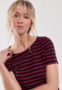 Marineblauwe t-shirt met rode horizontale strepen, ronde halslijn, korte mouwen en een zachte textuur. Heeft een relaxte pasvorm.