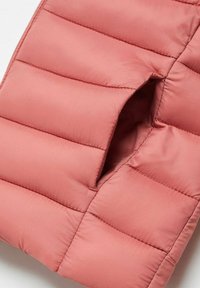 Vaate vaaleanpunaisesta pehmeästä liivistä, jossa on tikattu kuvio, suuri hihansuu ja sileä kangastuntuma.