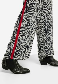 Zwart-witte zebra print broek met een rode zijstreep, gecombineerd met zwarte gestudeerde enkellaarsjes met een lage hak.