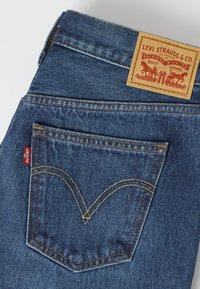 Τσέπη μπλε τζιν denim με το χαρακτηριστικό ραφτό arcuate της Levi's, κόκκινη ετικέτα Levi's και δερμάτινη ετικέτα Levi Strauss & Co. στη μέση.