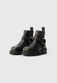 Botas de cuero negras hasta el tobillo con punta redondeada, detalle de hebilla de metal, paneles laterales elásticos y una suela gruesa de goma negra.