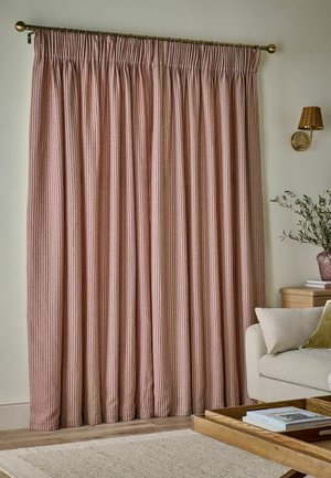 Tende chiuse a righe rosse e bianche appese a un'asta in ottone in un soggiorno con un divano beige, un tavolo in legno e una lampada a parete.