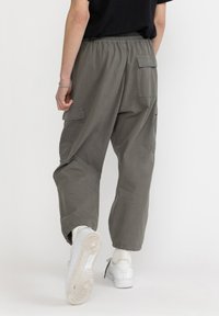 Olijfgroene cargo pants met een elastische tailleband, zijzakken en een relaxed fit. Gestyled met witte sneakers en een zwart shirt.