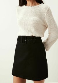 Maglione bianco a maglia testurizzata con scollo rotondo e gonna in denim nera con una cintura ampia e chiusura a fibbia.