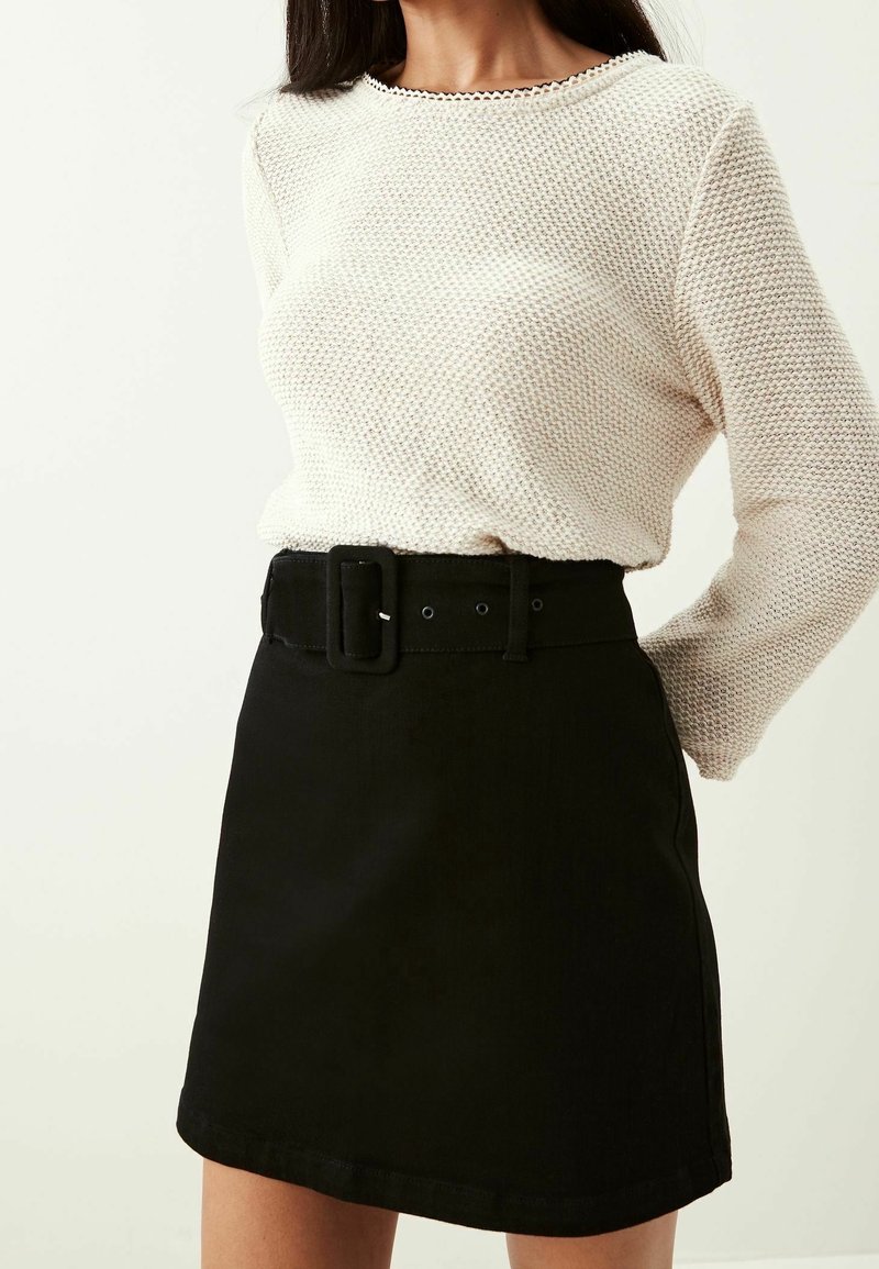 Maglione bianco a maglia testurizzata con scollo rotondo e gonna in denim nera con una cintura ampia e chiusura a fibbia.
