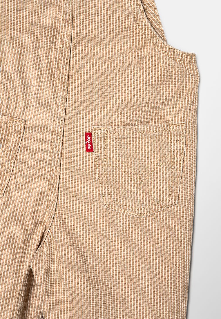 Beige gestreifte Latzhose aus strapazierfähigem Material; verfügt über eine Vordertasche und ein rotes Levi's Etikett an der Seite. Texturiert mit vertikalen Linien.
