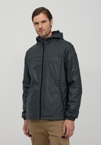 Giacca impermeabile grigia scura con cappuccio, zip frontale e polsini elastici. Presenta tasche laterali e una trama elegante e liscia.