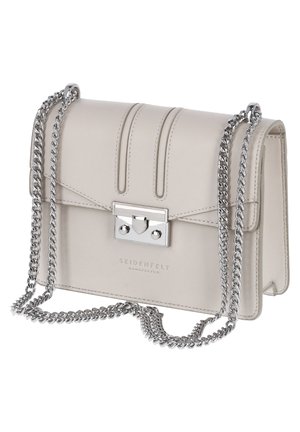 Pieni beige nahkainen olkalaukku, jossa on hopeinen ketjuhihna ja suorakaidehopeinen solki, etuosassa prässätty teksti "Seidenfelt Manufaktur".