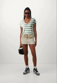 Groen en wit gestreepte V-hals t-shirt, beige mini rok met riem, zwarte handtas en sneakers. Glad materiaal met een casual pasvorm.