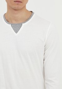 Langærmet T-shirt med et hvidt ydre lag, et gråt indre lag med V-udskæring og kontrasterende hvid syning. Blødt, letvægtsstof.