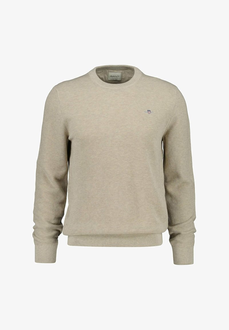 Pull beige en maille avec encolure ronde, poignets et ourlet côtelés, orné d'un petit logo brodé sur la poitrine. Tissu texturé.