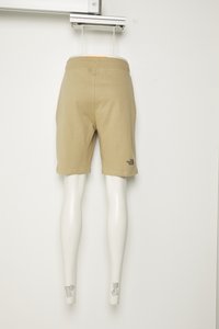 Pantaloni corti beige in cotone con vita elasticizzata, caratterizzati da un piccolo logo nero sulla gamba sinistra. Esibiti su un manichino bianco.